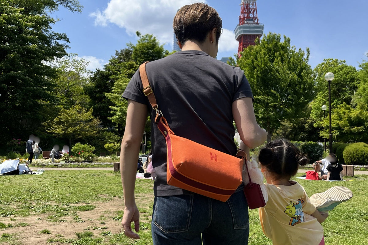 公園でオレンジのバッグをショルダーで掛けた着用イメージ